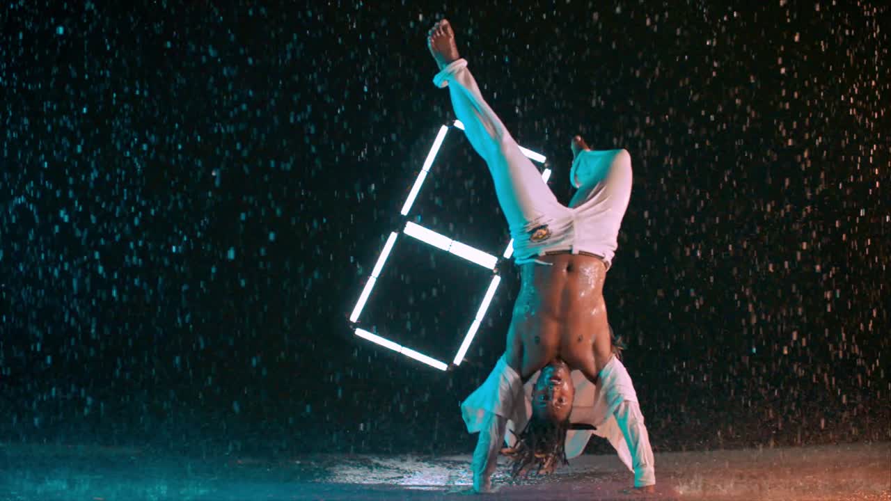 Capoeira dancer performing amazing spinning jump in the rain in super slow motion