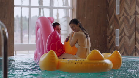 joyful-man-and-woman-are-riding-funny-inflatable-swimming-circles-splashing-water-and-having-fun