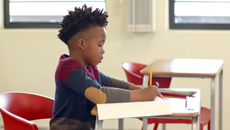 in school, young african american boy attentively writing in notebook at classroom desk
