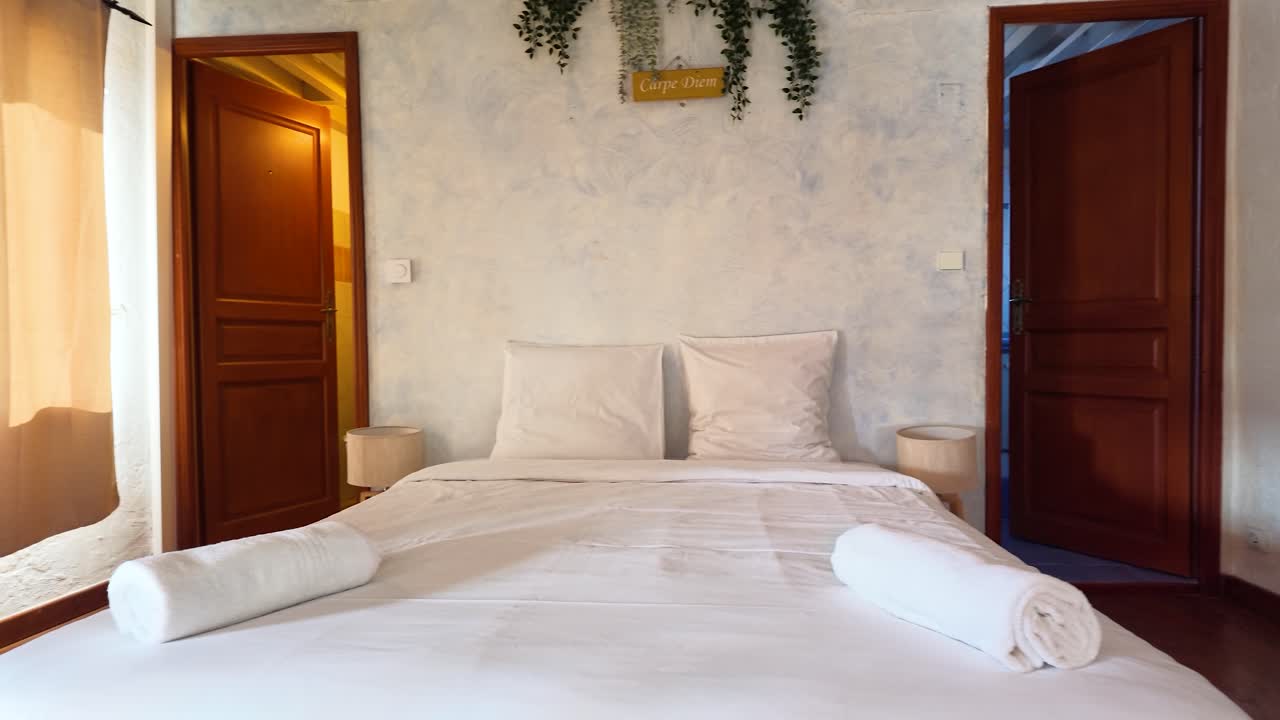 Een langzame camerapan onthult een rustieke Franse slaapkamer met wit beddengoed en vintage meubels.
