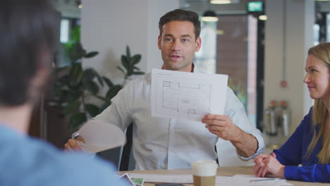 equipo de arquitectos reunidos alrededor de una mesa discutiendo el plan en una oficina moderna de plan abierto