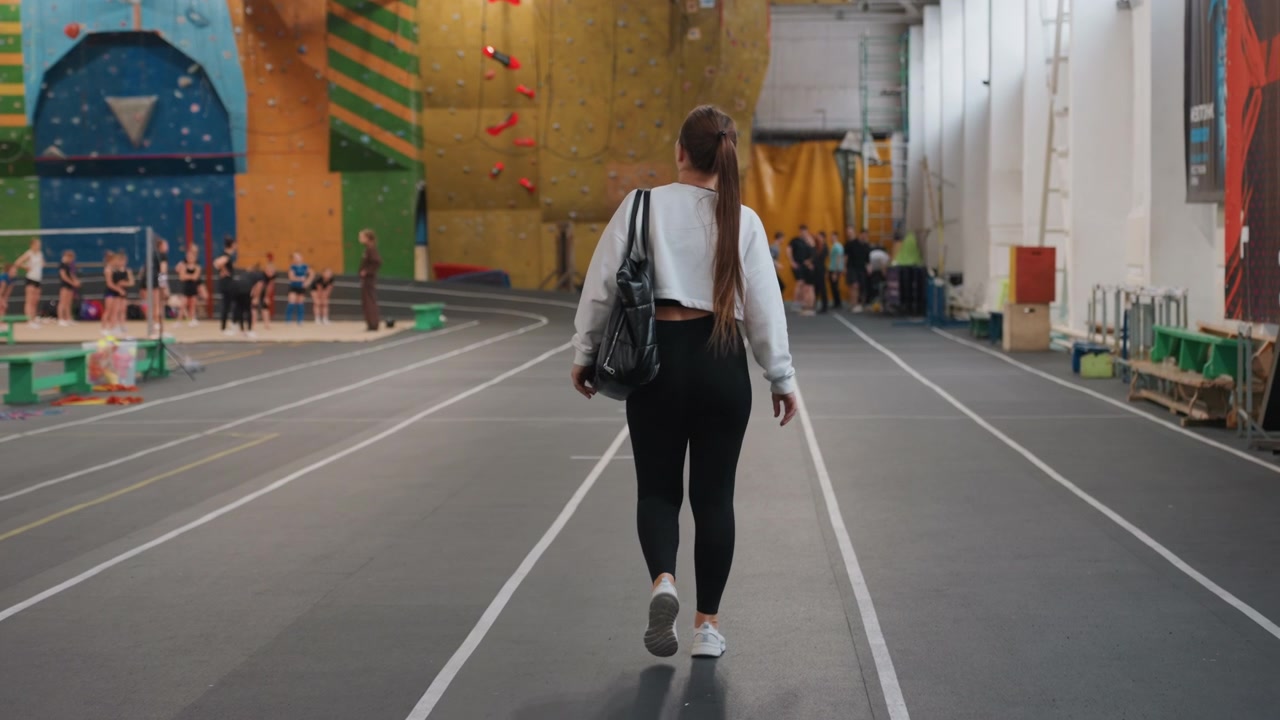 Participant steadily heads toward sports area. Competitor calmly navigates corridor to fitness zone. Individual purposefully advances through gym past climbing apparatus and equipment