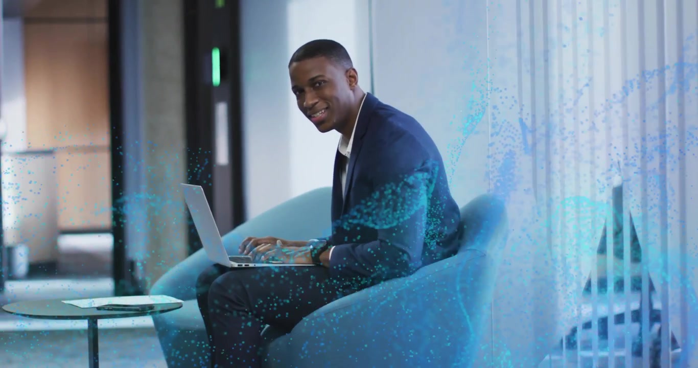Man typing on laptop activating blue particles turning to camera engaging audience in tech demo