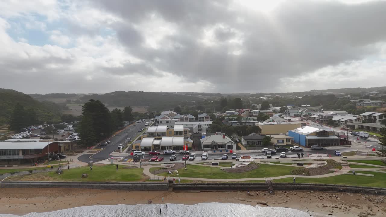 Aerial footage captures Port Campbell's coastal town under cloudy skies, showcasing buildings, roads, and the ocean in a serene setting