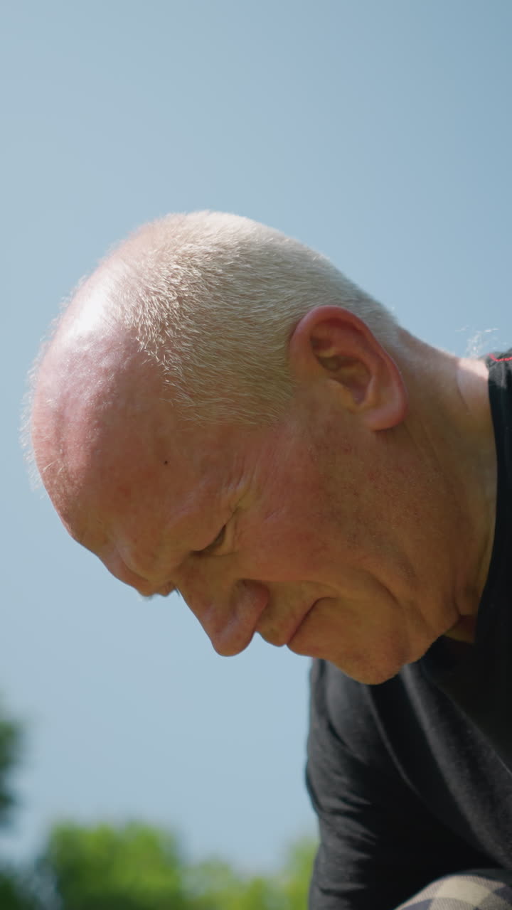 한 노인이 무을 고, 작업에 깊이 집중하고, 머리를 약간 들어 올리며, 배경에는 은 하늘 아래의 나무의 흐릿한 특징이 있습니다.