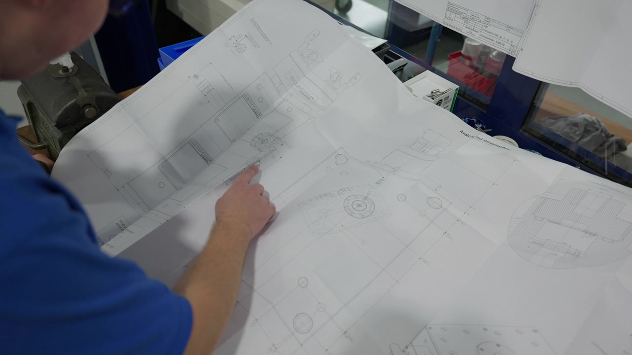 Closeup of engineer studying blueprint schematic and technical drawing on paper reviewing dimensions and planning machine fabrication and manufacturing workflow in workshop