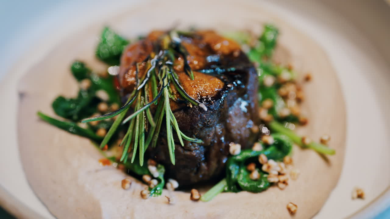 Close up of a beautifully plated beef filet, topped with a golden crust and garnished with rosemary