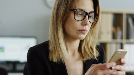 Close-Up-Of-The-Busy-Beautiful-Businesswoman-In-Glasses-Taping-And-Texting-On-Her-Smartphone-In-The-Office
