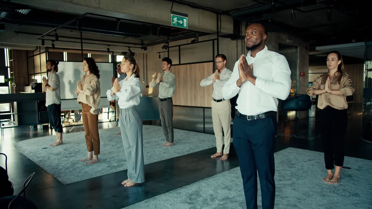The team in the office is engaged in meditation and yoga. Office workers stand on the carpet and fold their hands in front of them in the office
