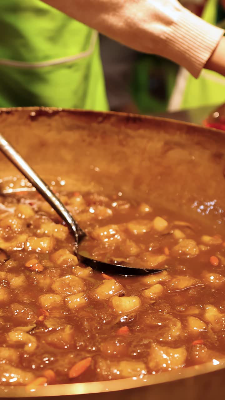 Vendedor servindo sopa quente de bucho de peixe em saco plástico sob a luz quente da comida de rua.