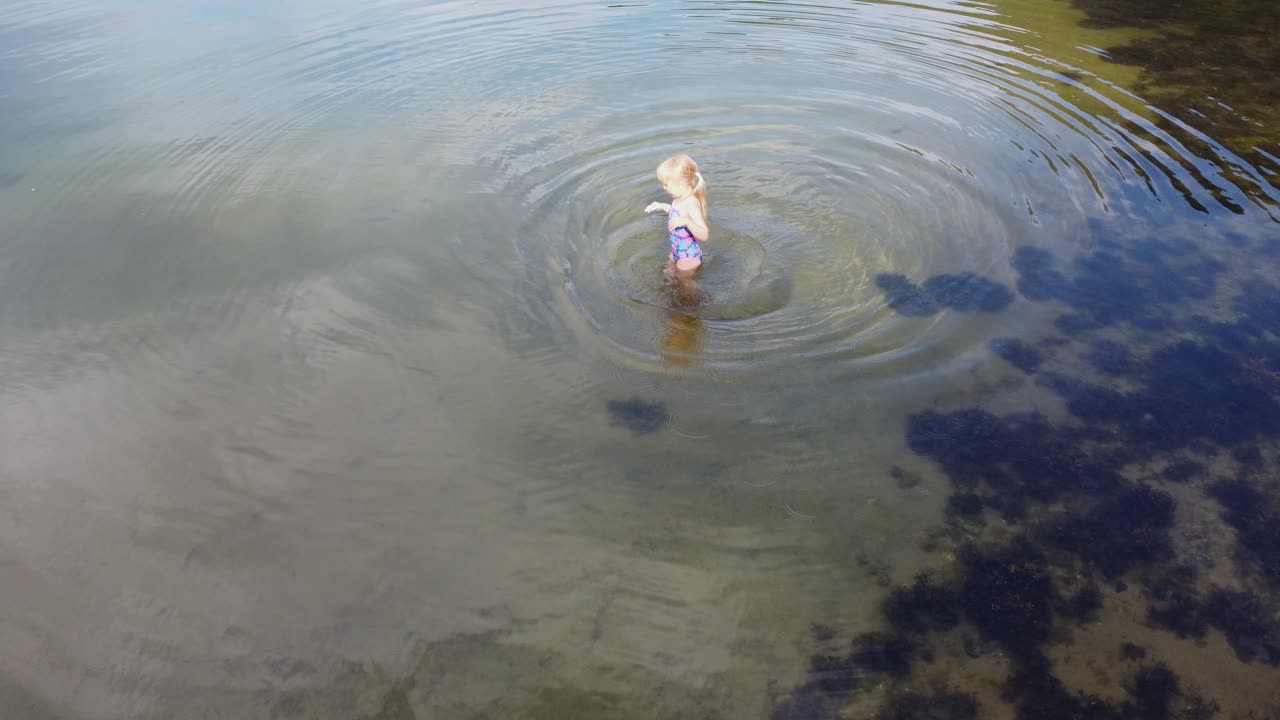 linda niña rubia jugando y divirtiéndose en el fiordo noruego durante las vacaciones de verano - la luz del sol golpea a la niña saltando sobre el fondo de arena - órbita aérea y pasando por encima del niño