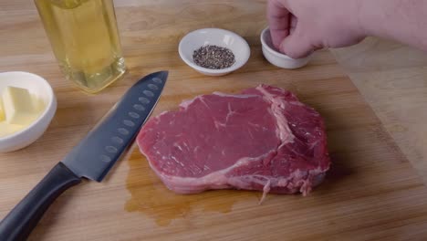 slow motion slider shot of seasoning a ribeye steak with salt on a wooden cutting board prior to cooking