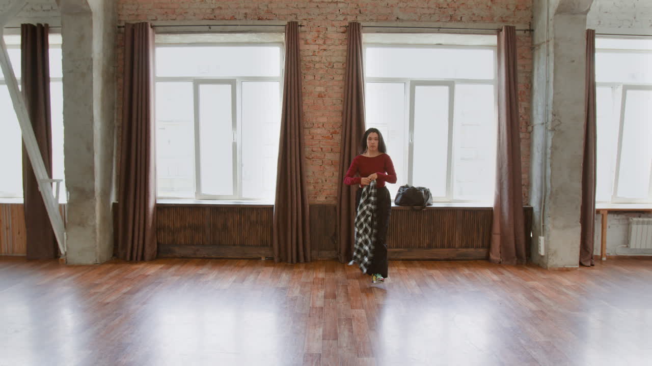 A woman stands in a large, bright studio space with brick walls and wooden floors