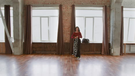 a woman stands in a large, bright studio space with brick walls and wooden floors