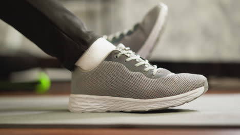 person in grey sneakers sitting on a yoga mat, exercising