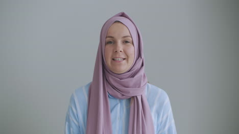 Looking-at-the-camera-muslim-girl-calling-friends-from-apartments-using-a-video-link-waving-with-hand-sitting-on-a-sofa-in-a-stylish-room-in-front-of-computer-screen-having-video-conversation