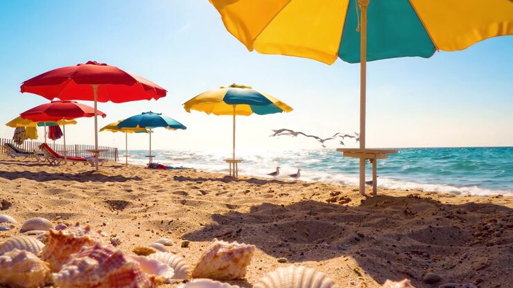 Una splendida giornata in spiaggia: Ombrelloni colorati e conchiglie sulla riva sabbiosa con onde scintillanti sotto un cielo sereno