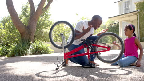 fixing bicycle, african american man teaching girl how to repair bike outdoors