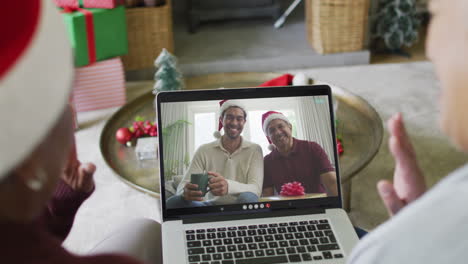 dos amigas mayores diversas que usan una computadora portátil para una videollamada de navidad con la familia en la pantalla