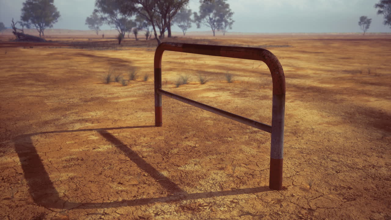 Rusty goal post stands alone in a dry cracked field under a cloudy sky