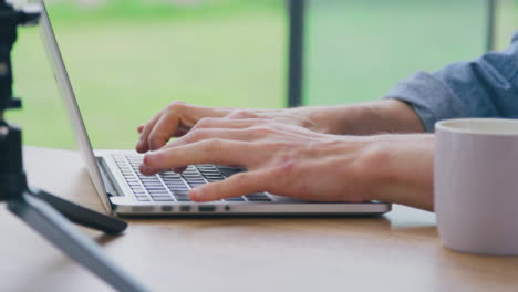 Close-Up-Of-Male-Vlogger-Wearing-Headphones-Typing-On-Laptop-With-Microphone-In-Foreground