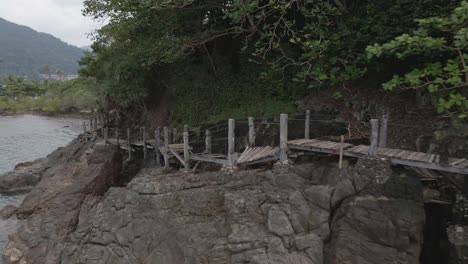 drone dolly shot of a broken wooden boardwalk on a granite rock coastline on a tropical island with jungle lush green forest and ocean