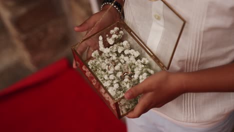 child holding a glass box with gold wedding rings and white flowers during ceremony