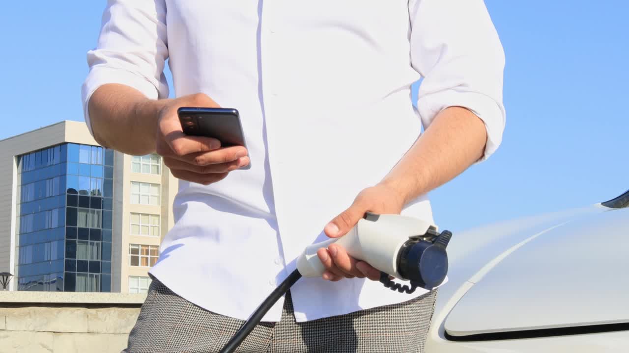 an adult man charges a car battery from a small public station, using a smartphone application