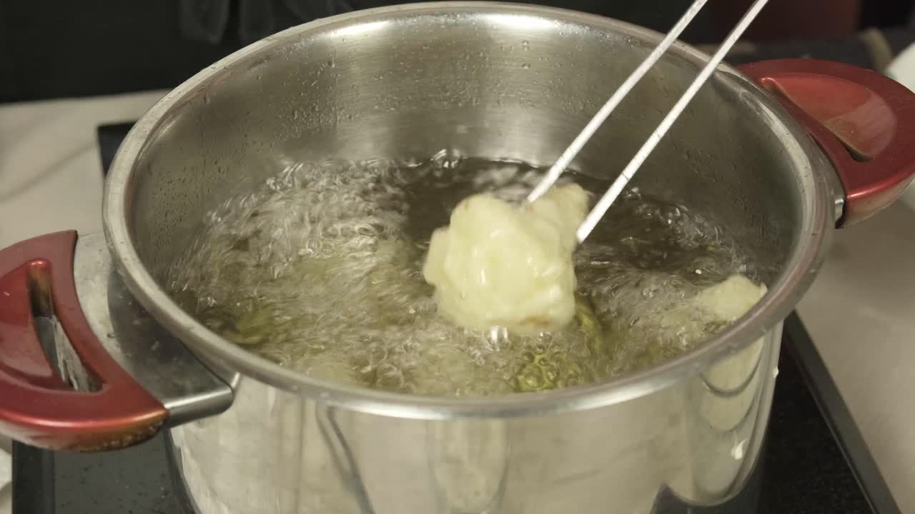 Kokk bruker metalltang for å sjekke frityrstekt brokkoli i en stor gryte med olje