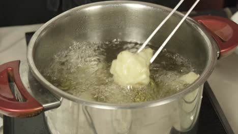 chef uses metal tongs to check on batter fried broccoli in large pot of oil