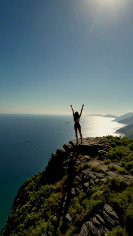 woman triumphantly overlooking a breathtaking ocean and mountain landscape from a cliff