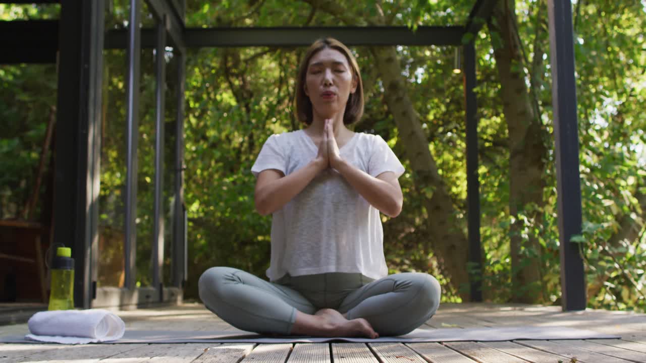 mujer asiática meditando y sentada en un tapete de yoga en el jardín