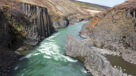 drone flight over a turquoise river flowing through a basalt column canyon in iceland