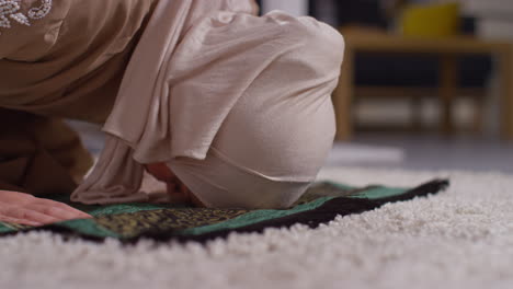 close up of muslim woman wearing hijab at home praying kneeling on prayer mat 6