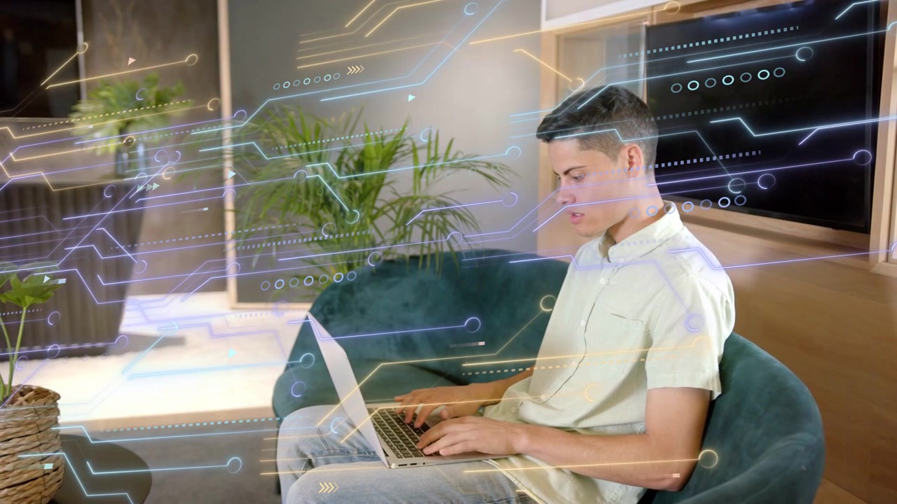 Man typing on laptop in teal chair, activating circuit overlay for tech designers, marketers