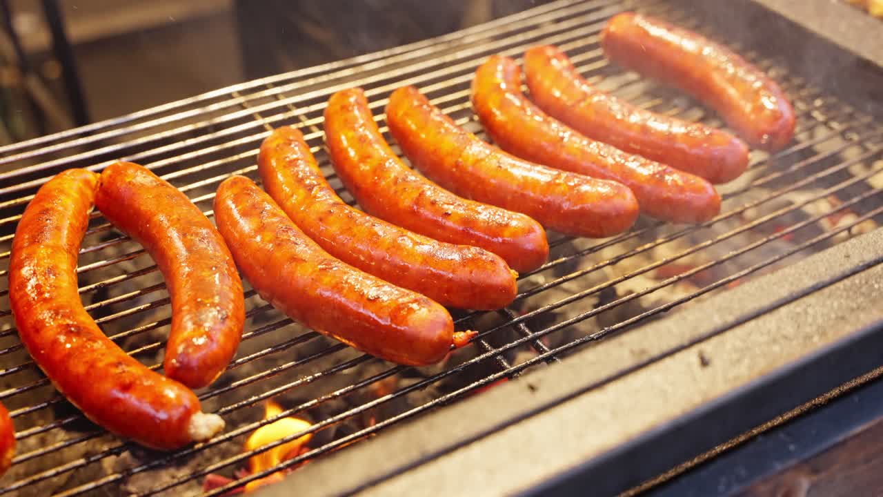 Golden sausages sizzling above hot metal grates with bright highlights and rich roasted surfaces