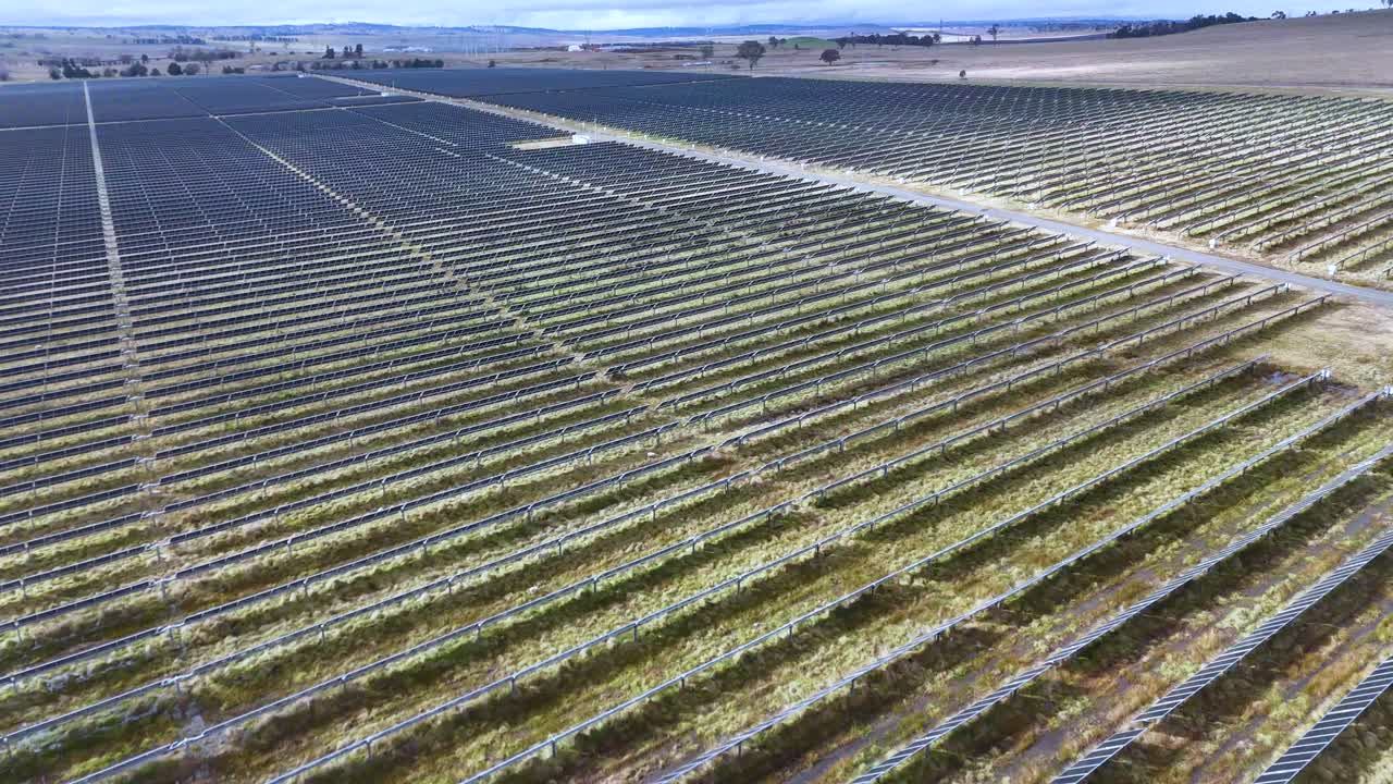 Drone camera glides above expansive solar cell array in rural New South Wales, Australia, under daylight with clear sky, capturing geometric panel patterns and landscape