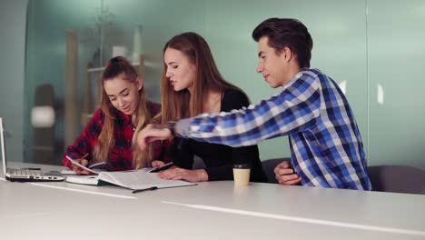 tres estudiantes trabajando en sus tareas sentados juntos en la mesa y bebiendo café. grupo de jóvenes en la reunión en un apartamento moderno. disparo en cámara lenta