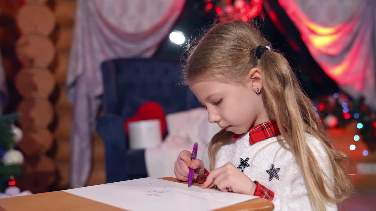 Little girl painting on Christmas tree background. Cute child drawing a picture to Santa before Christmas. New Year tree with bright lights in the room.