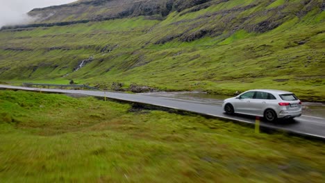 a car drives on a remote road surrounded by lush green hills in the faroe islands