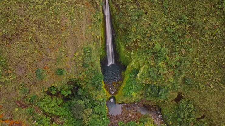 An breathtaking aerial view reveals the unique and beautiful Vuelta al Cañon waterfall, cascading majestically into a vibrant, untouched green canyon