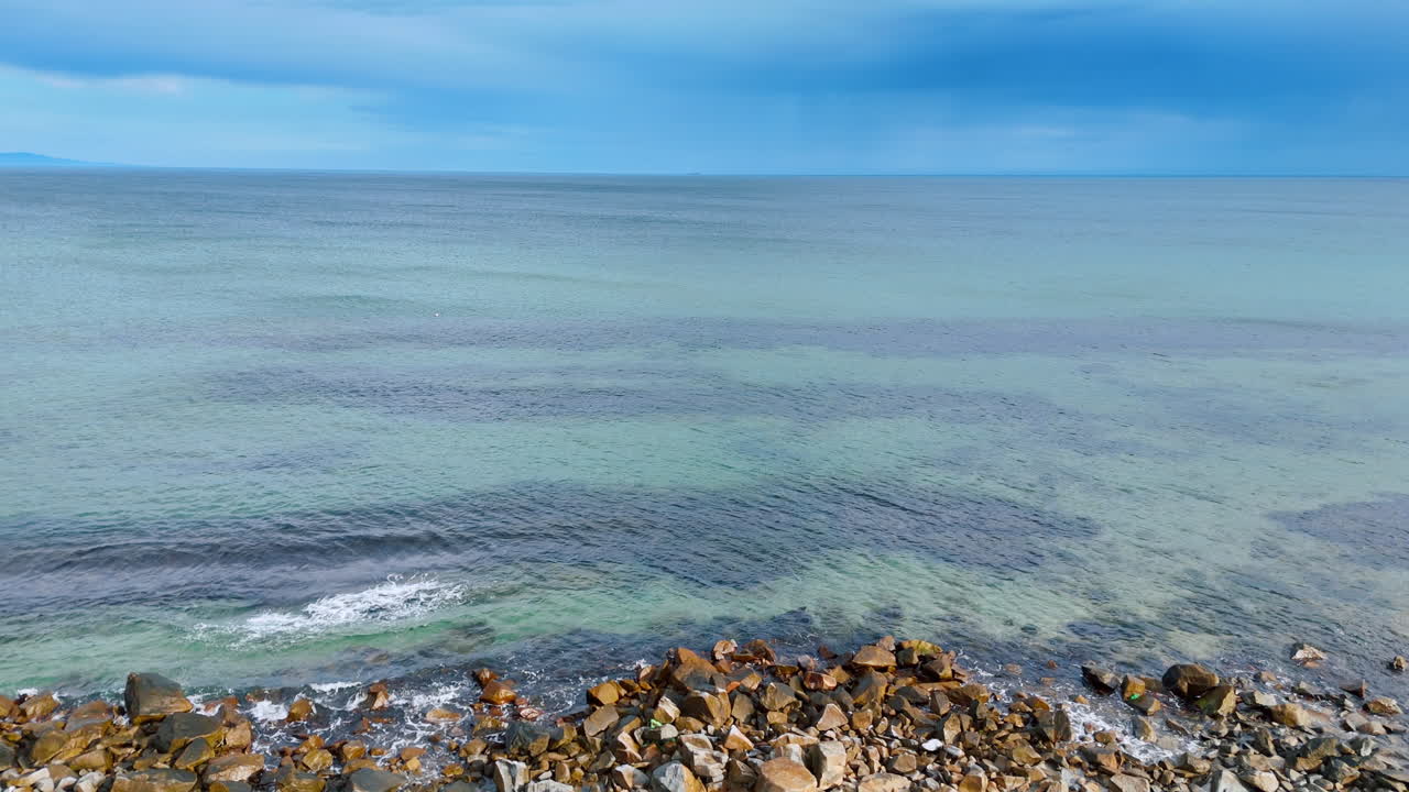 Littoral rocheux avec des galets et de l'eau de mer transparente. Vue en contre-plongée d'une plage caillouteuse passant à l'eau claire de l'océan sous un ciel nuageux et sombre.