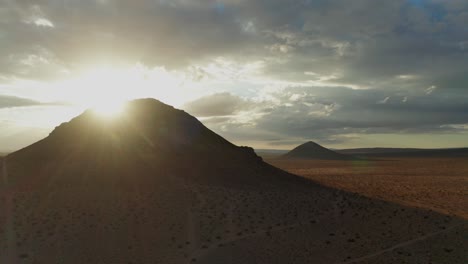 Aerial,-sun-shining-through-storm-clouds-behind-Mojave-Desert-mountain