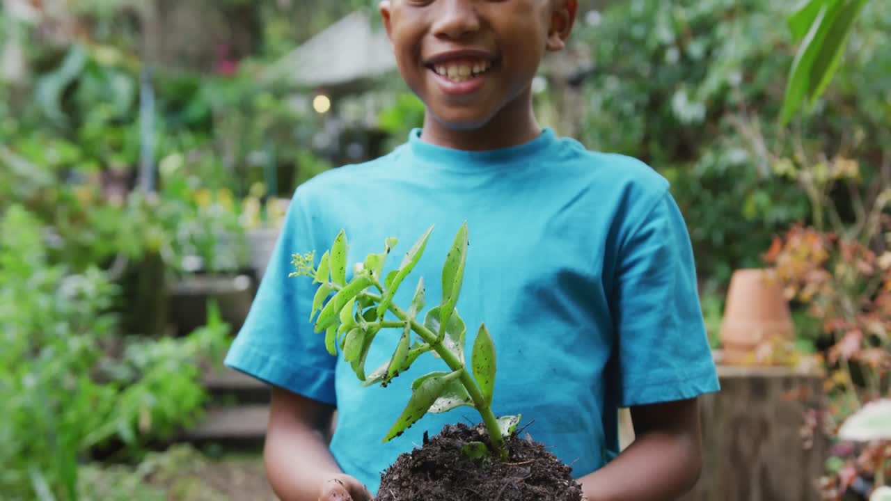 retrato de un feliz niño afroamericano sosteniendo una planta en el jardín