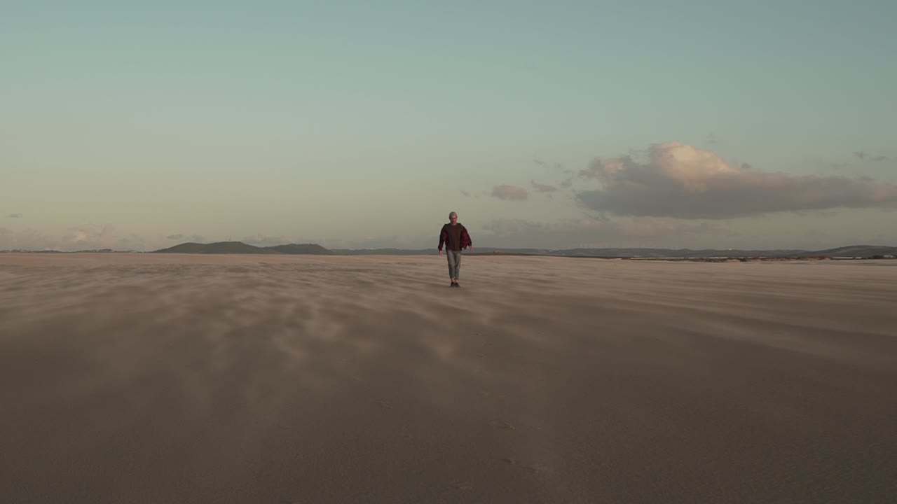 hombre caminando por la playa de arena al atardecer