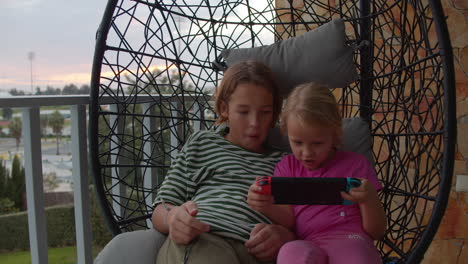 siblings bonding over gaming in portable console on a swing chair