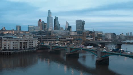 Toma-De-Un-Dron-De-Grúa-En-Ascenso-De-Los-Icónicos-Rascacielos-De-Londres-Y-El-Río-Támesis-Al-Atardecer