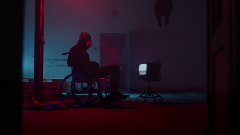 man in wheelchair watching tv in a desolate, neon-lit building