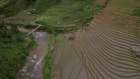 Aerial-perspective-of-terraced-rice-fields-near-the-river-in-Sa-Pa,-nestled-within-Vietnam's-Hoàng-Liên-Son-Mountains