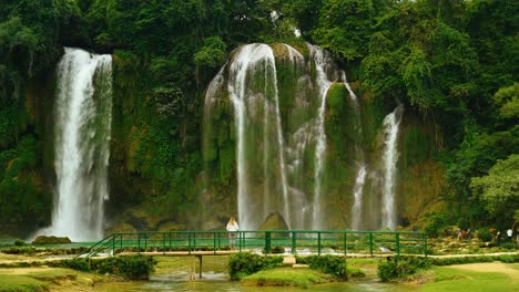 parallax view of young tourist woman standing on a bridge in front of giant bao gioc waterfall looking at waterfall